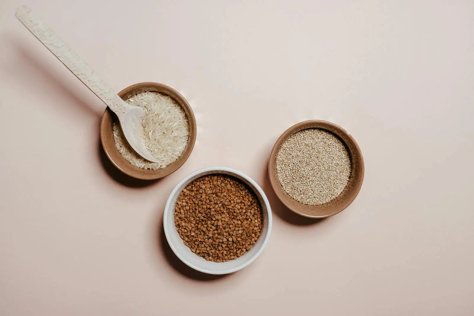 Bols de céréales et graines sans gluten — riz, quinoa, sarrasin et millet — disposés sur un plan de travail en bois