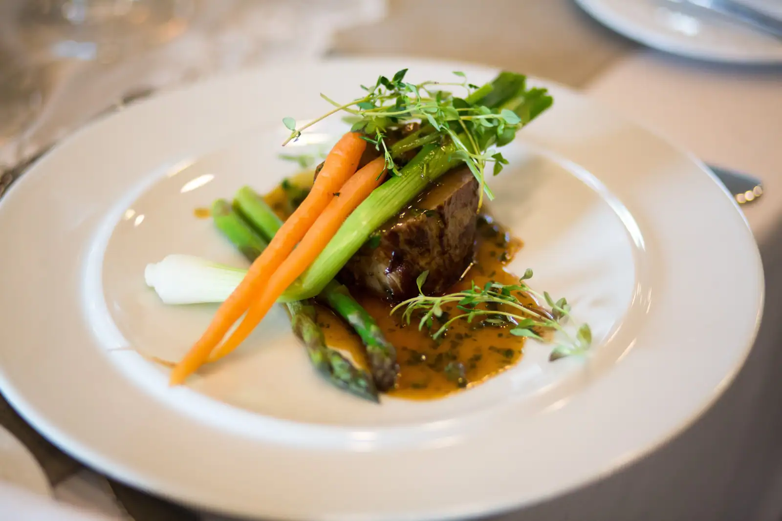 Plat gastronomique dressé dans une assiette blanche : viande, légumes et sauce dans un cadre raffiné