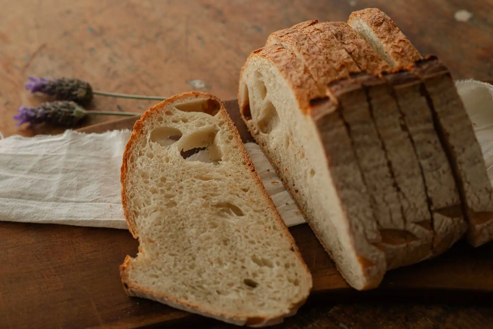 Pain de campagne tranché sur une planche en bois, posé sur un linge avec quelques brins de lavande.