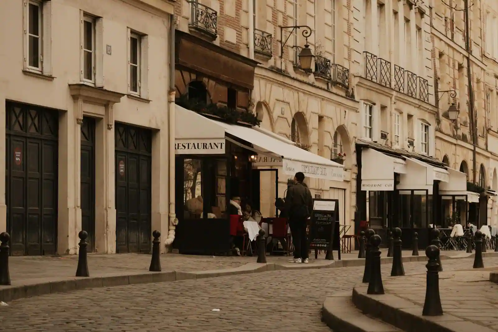 Terrasse d'un café-restaurant parisien, avec stores et tables, le long d'une rue pavée