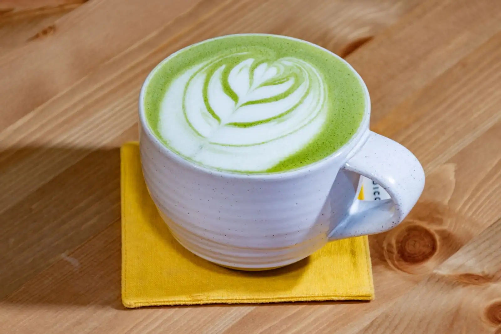 Matcha latté à l'art latté en feuille dans une tasse blanche posée sur une table en bois
