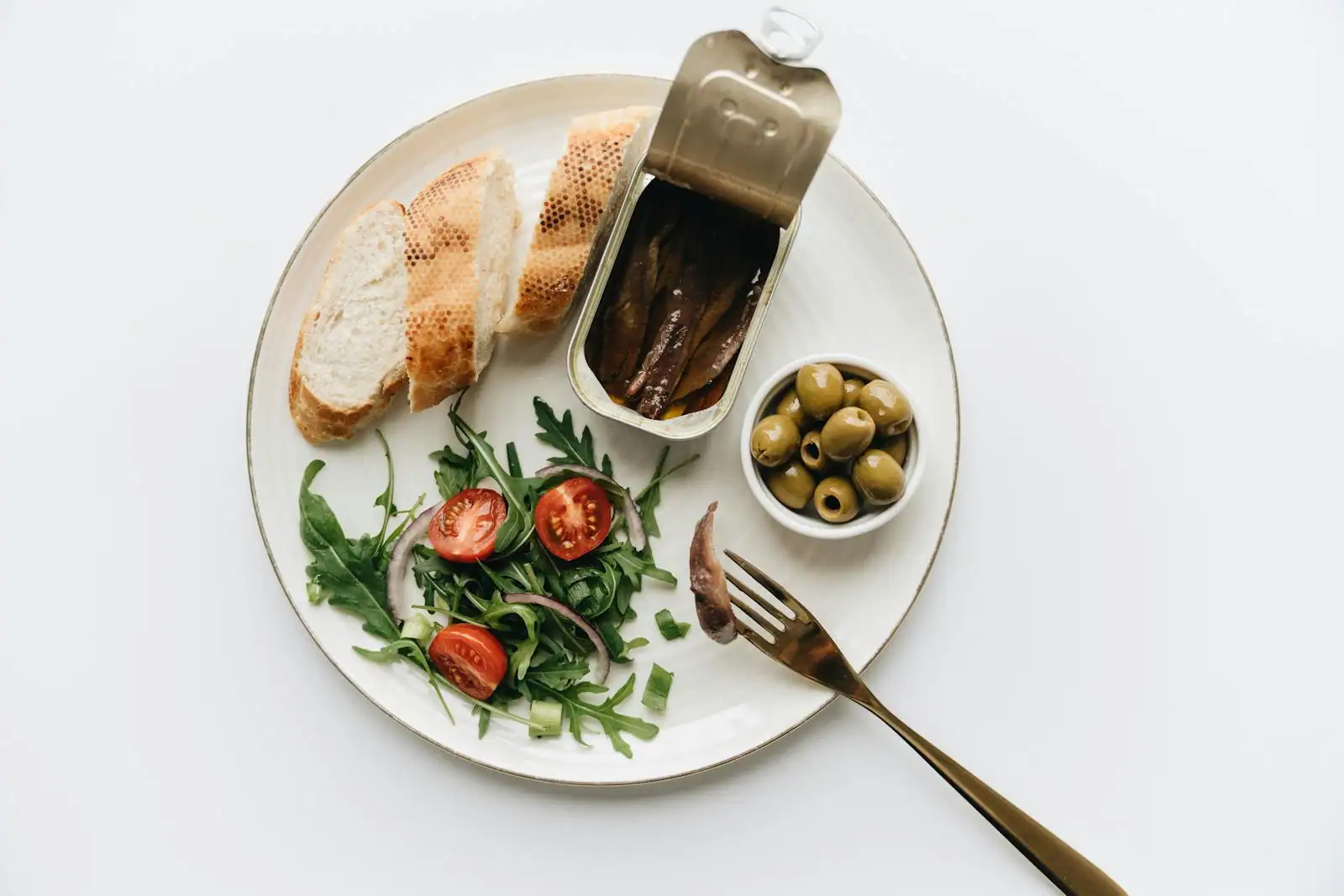 Repas méditerranéen avec pain, olives, anchois et salade de tomates et roquette