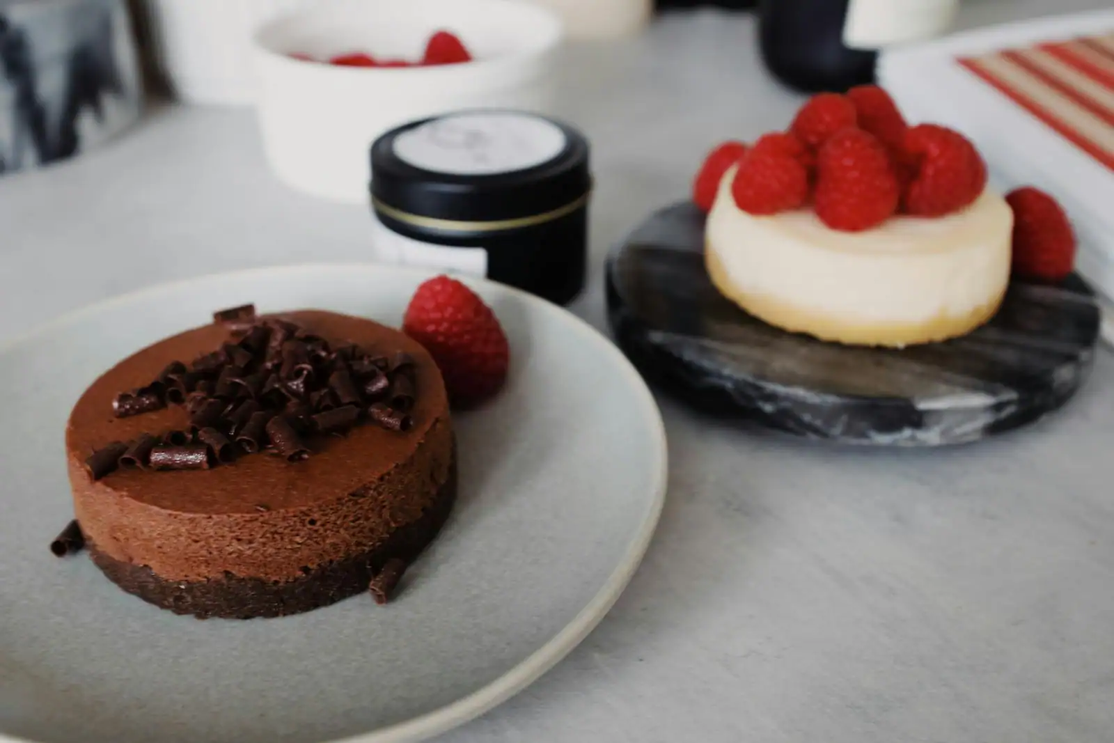 Petit gâteau au chocolat garni de copeaux et d'une framboise sur une assiette, dessert aux framboises en arrière-plan