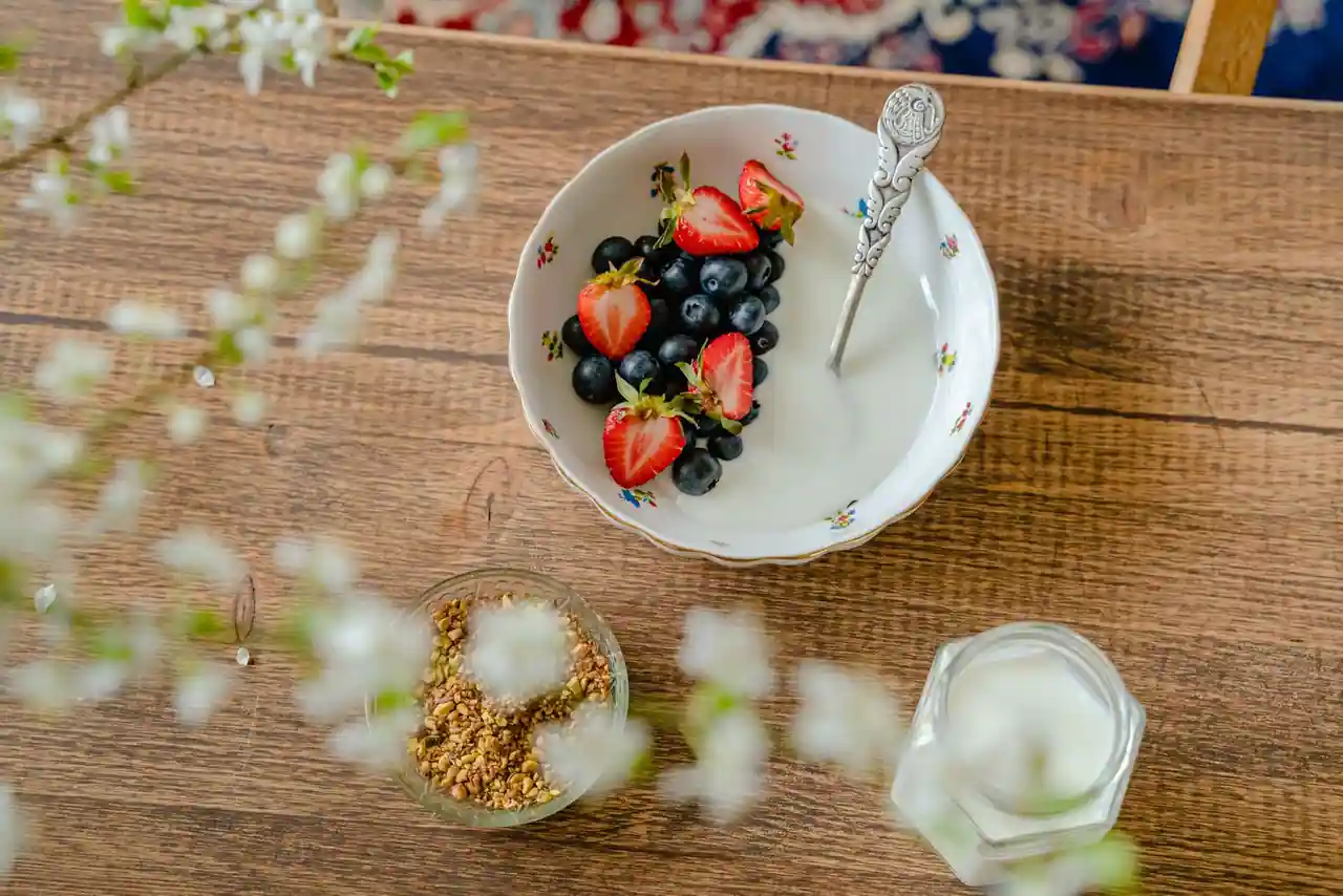 Bol de yaourt garni de fraises et de myrtilles, accompagné de granola, sur une table en bois