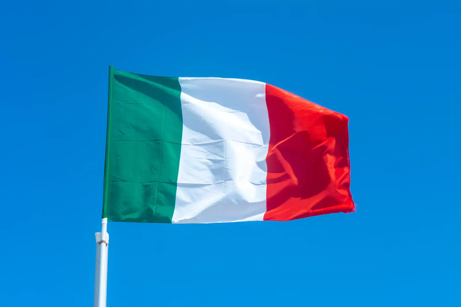 Drapeau italien aux trois bandes verticales verte, blanche et rouge, flottant sur un mât devant un ciel bleu