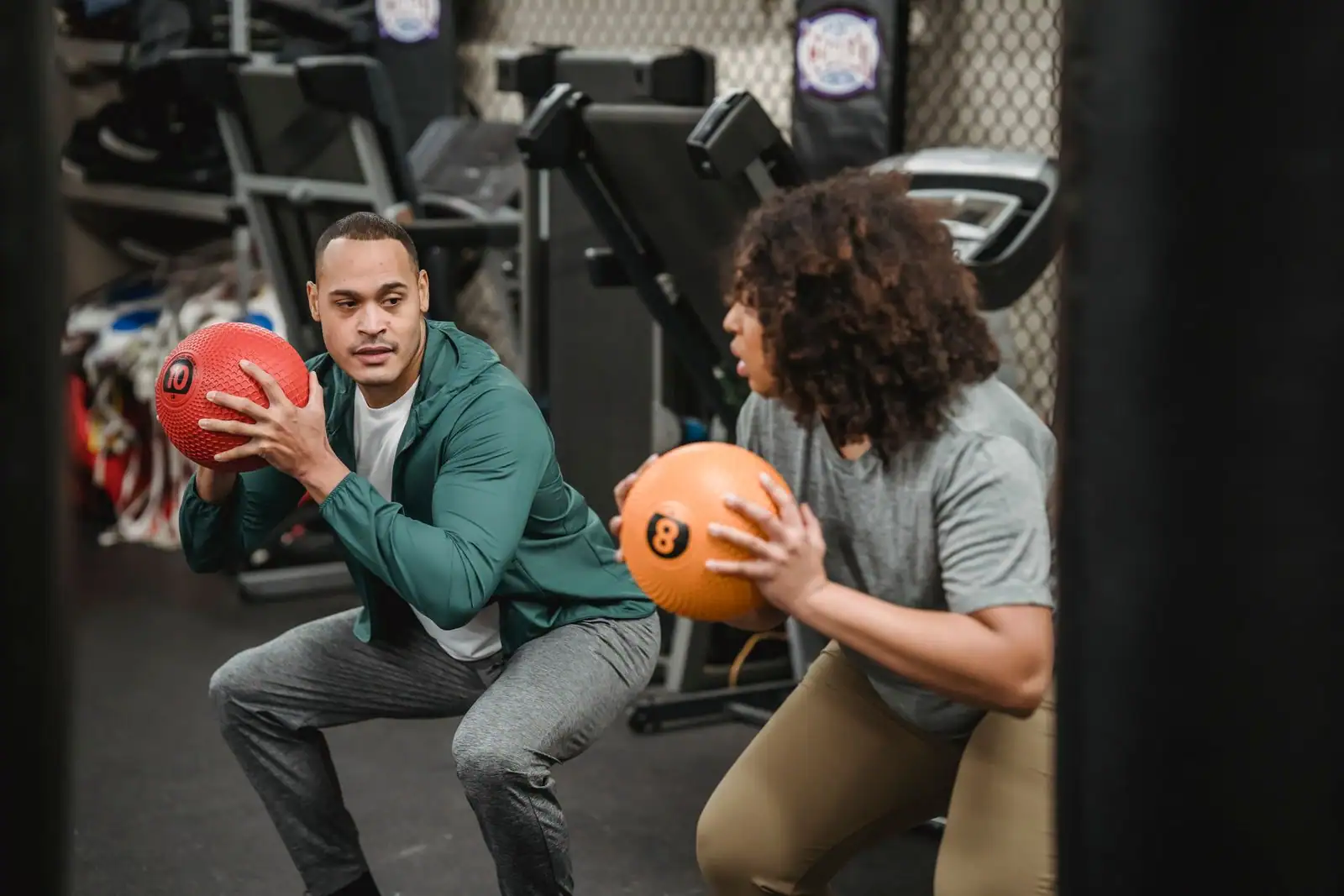 Deux sportifs en salle réalisent des squats en tenant chacun un ballon lesté