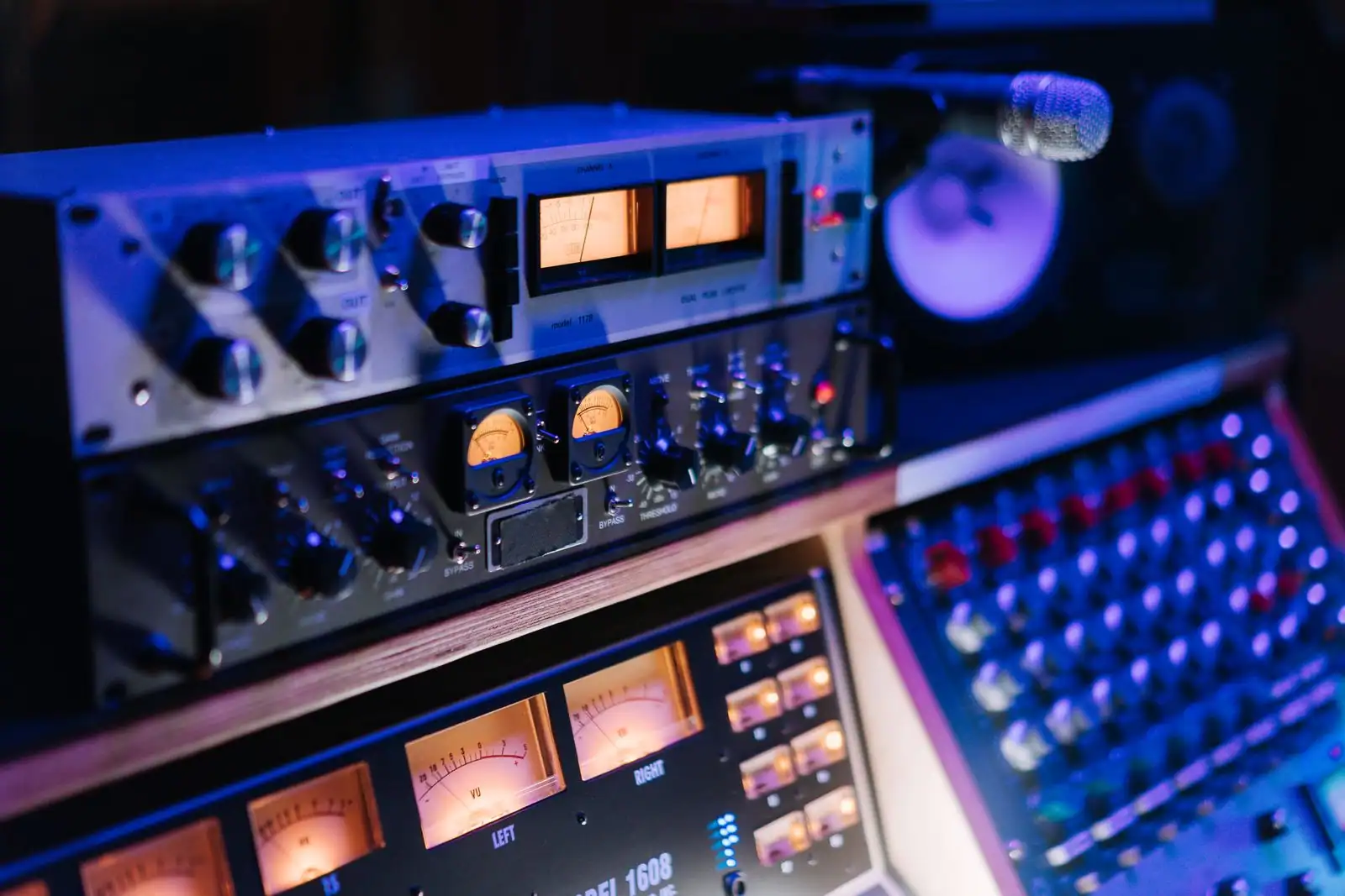 Matériel de studio audio — processeurs à vumètres, microphone et console de mixage — sous une lumière bleutée