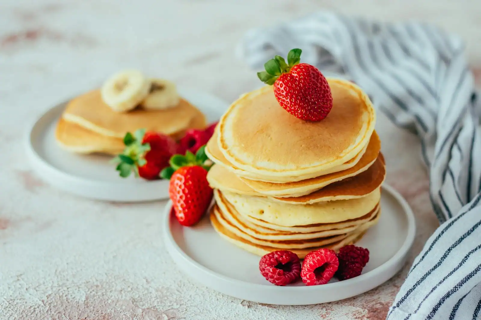 Pile de pancakes dorés garnis de fruits rouges et de banane sur une assiette