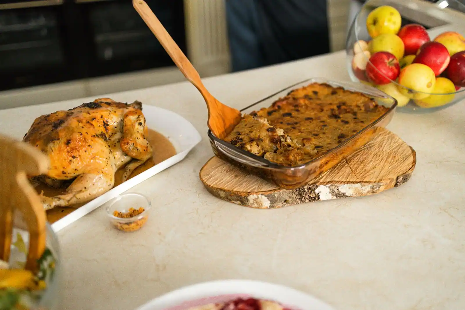 Poulet rôti et plat gratiné doré dans un plat en verre, avec une coupe de pommes, sur un plan clair