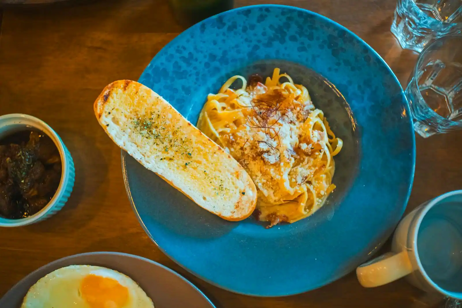 Une assiette de spaghetti crémeux façon carbonara, parsemés de fromage râpé et servis avec une tranche de pain grillé.