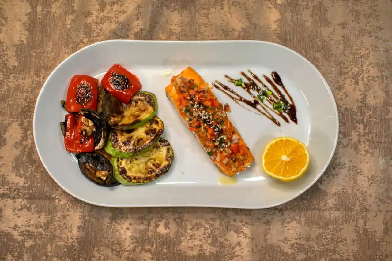 Pavé de saumon et légumes grillés colorés — tomate, courgette, aubergine — dans une assiette blanche