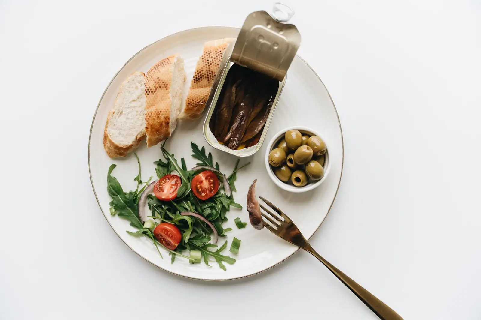Assiette méditerranéenne avec pain, salade de roquette et tomates, olives vertes et anchois