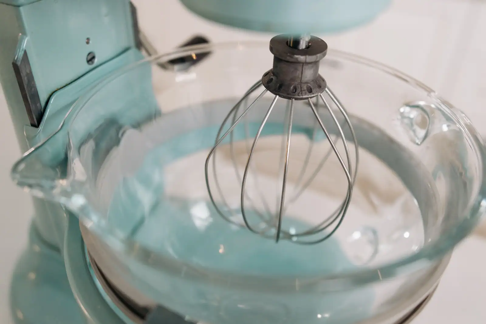 Gros plan d’un robot pâtissier équipé de son fouet ballon, au-dessus d’un bol en verre