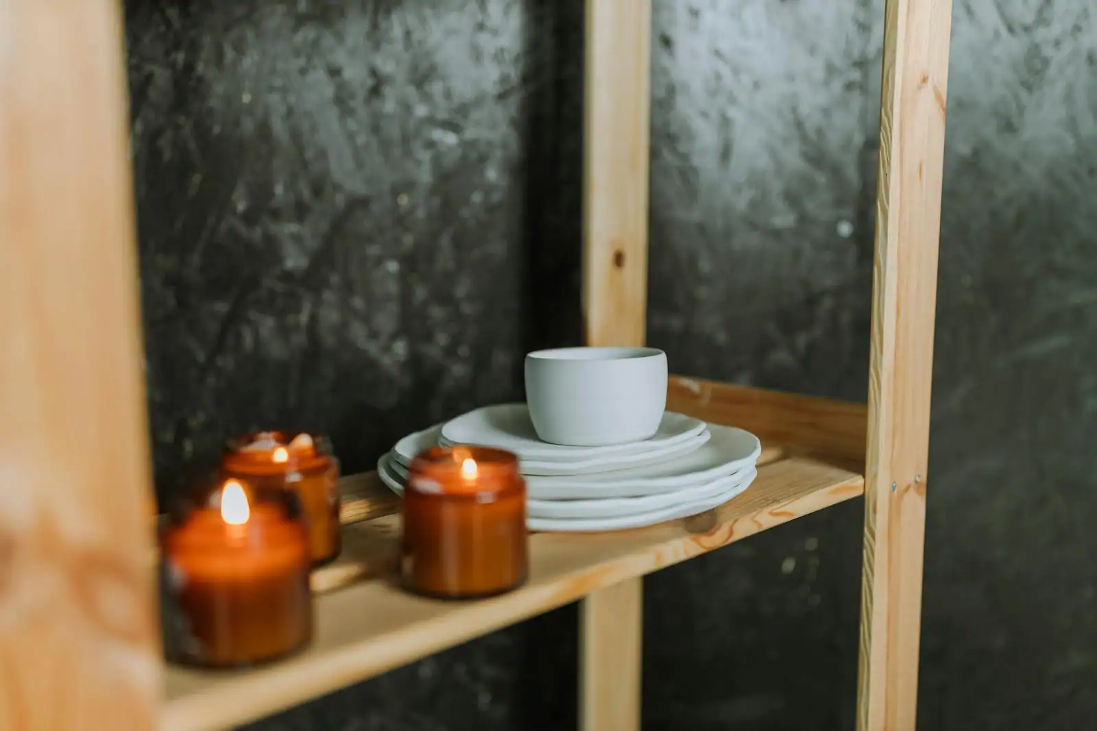 Une pile d'assiettes blanches surmontée d'un bol en céramique, posée sur une étagère en bois.