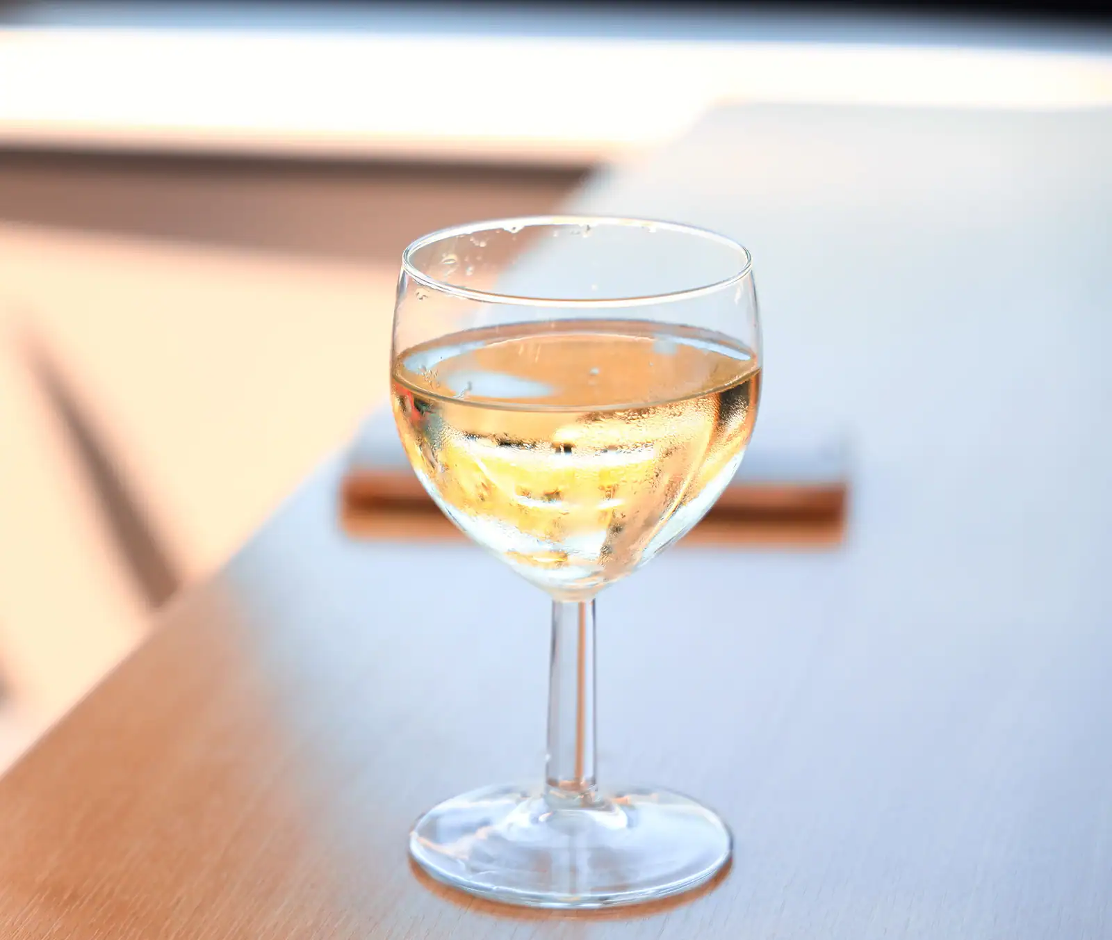 Verre de vin blanc à la robe dorée posé sur une table en bois, dans une lumière douce