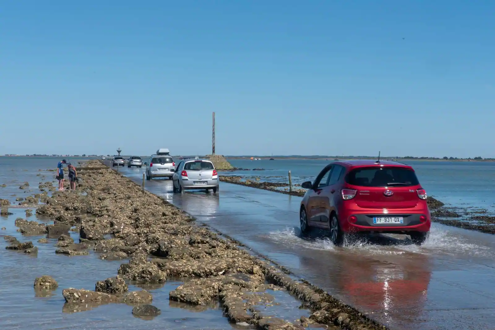 Voitures traversant le passage du Gois à marée basse, entre les rochers découverts et l'eau basse.