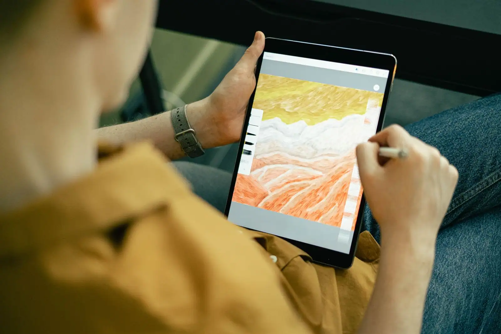 Tablette tenue à la main, stylet en action sur une application de dessin numérique.