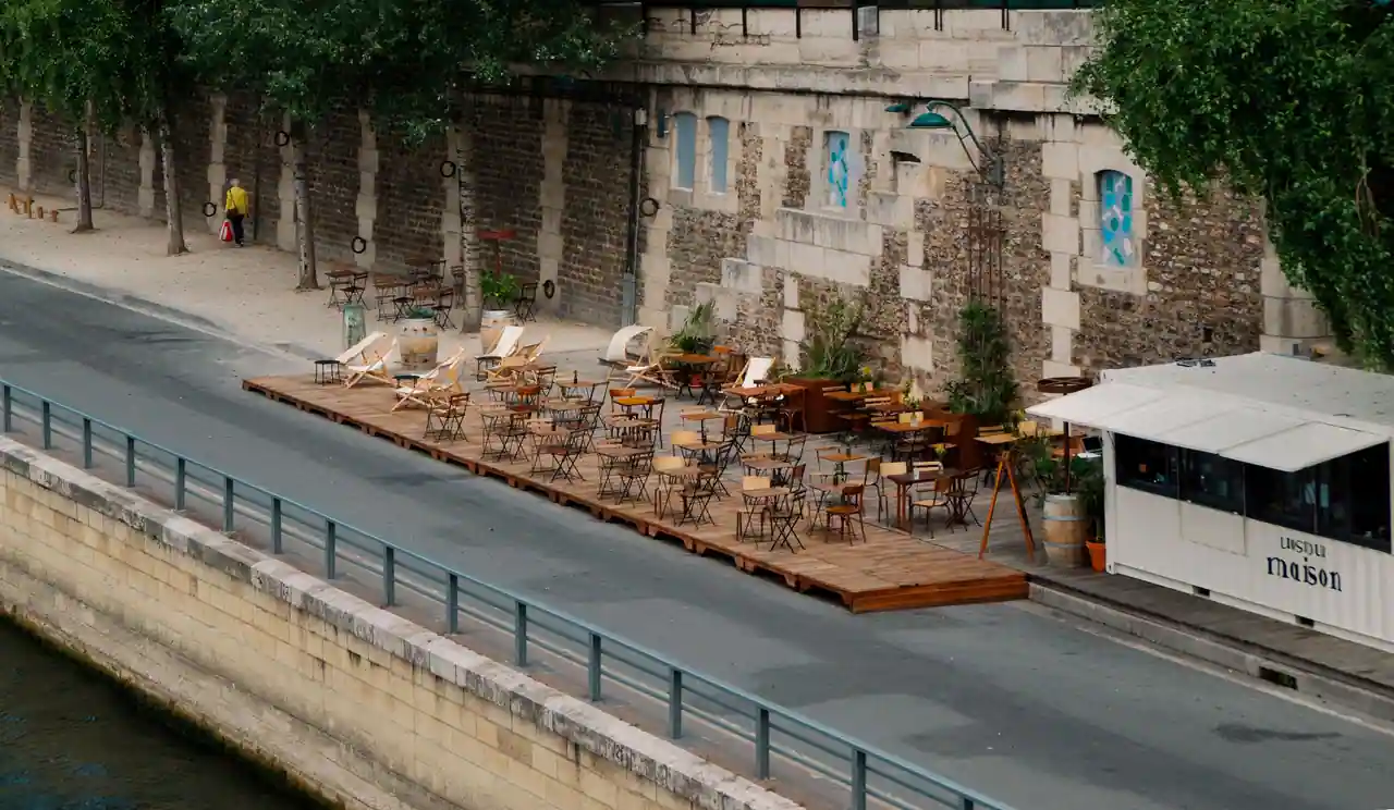 Terrasse de café parisienne installée sur un ponton de bois le long des quais de la Seine, chaises vides