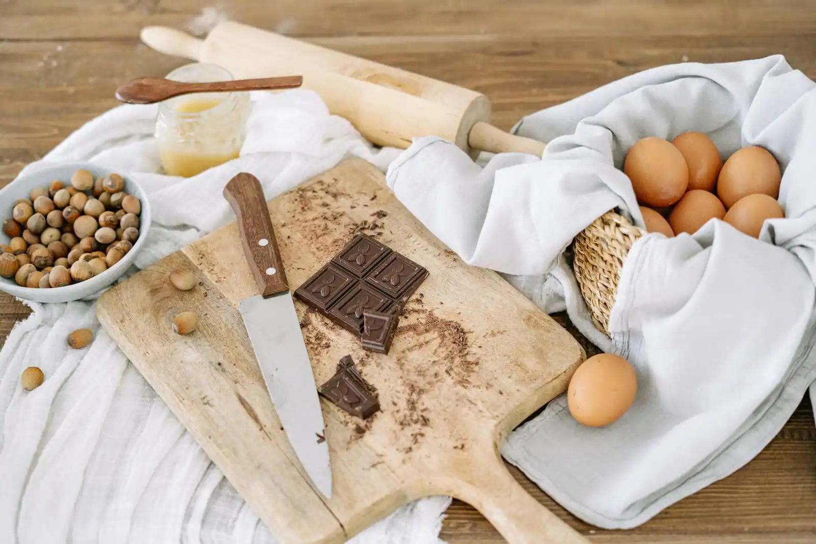 Tablette de chocolat entamée sur une planche, à côté d'œufs et de noisettes, avant préparation