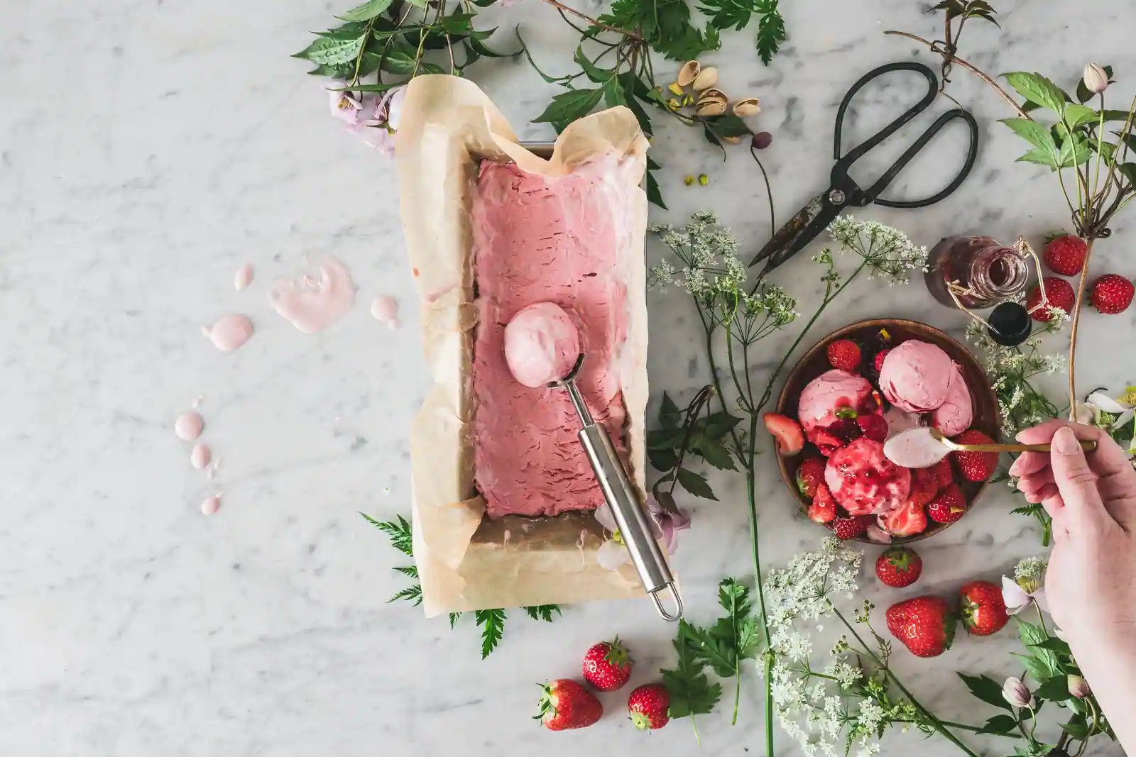 Glace maison rose prise dans un moule chemisé de papier, cuillère à glace et coupelle de boules aux fraises