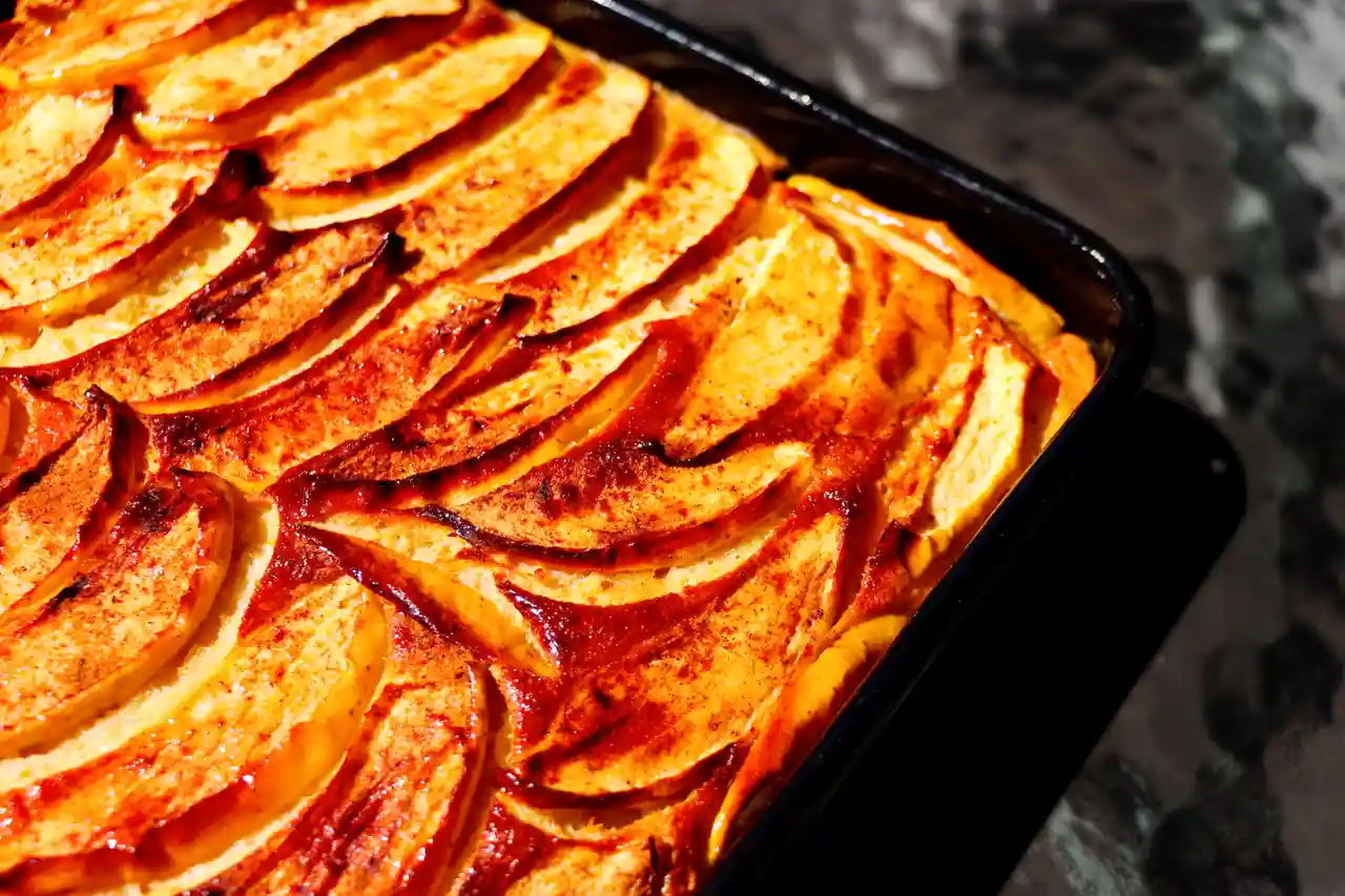 Lamelles de pommes dorées et caramélisées sur un gâteau cuit au four, dans un plat rectangulaire