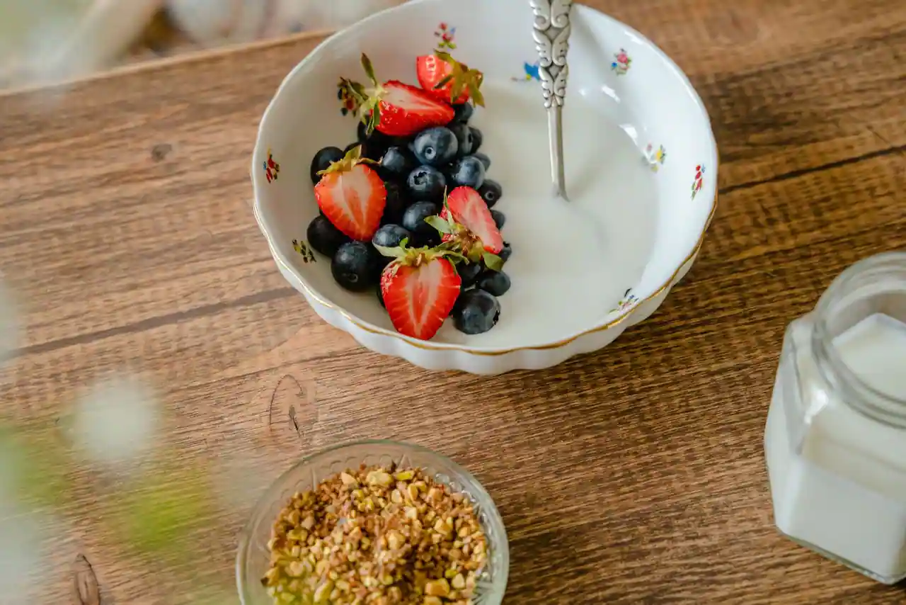 Bol de laitage nature garni de fraises et de myrtilles fraîches, avec une cuillère, sur une table en bois.