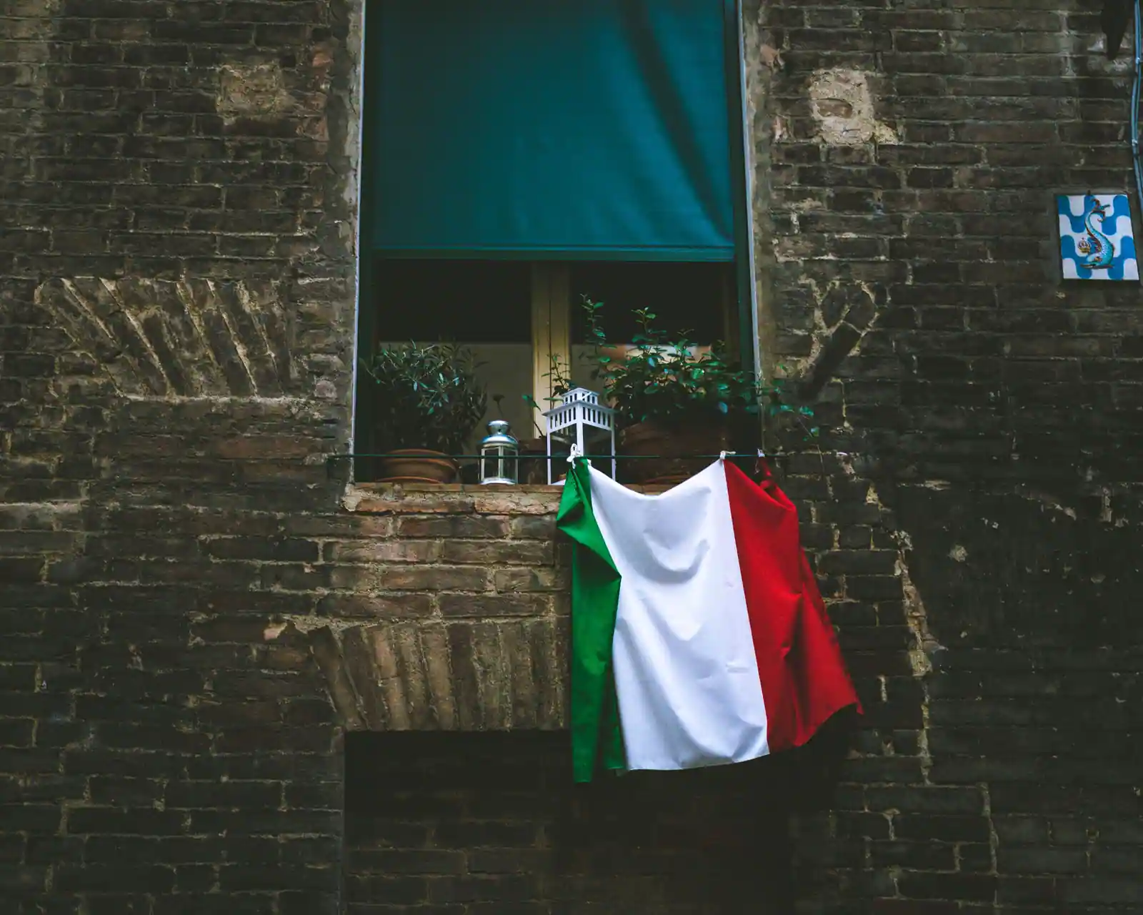 Drapeau italien vert blanc rouge suspendu à la fenêtre d'un vieux bâtiment de briques, plantes au rebord