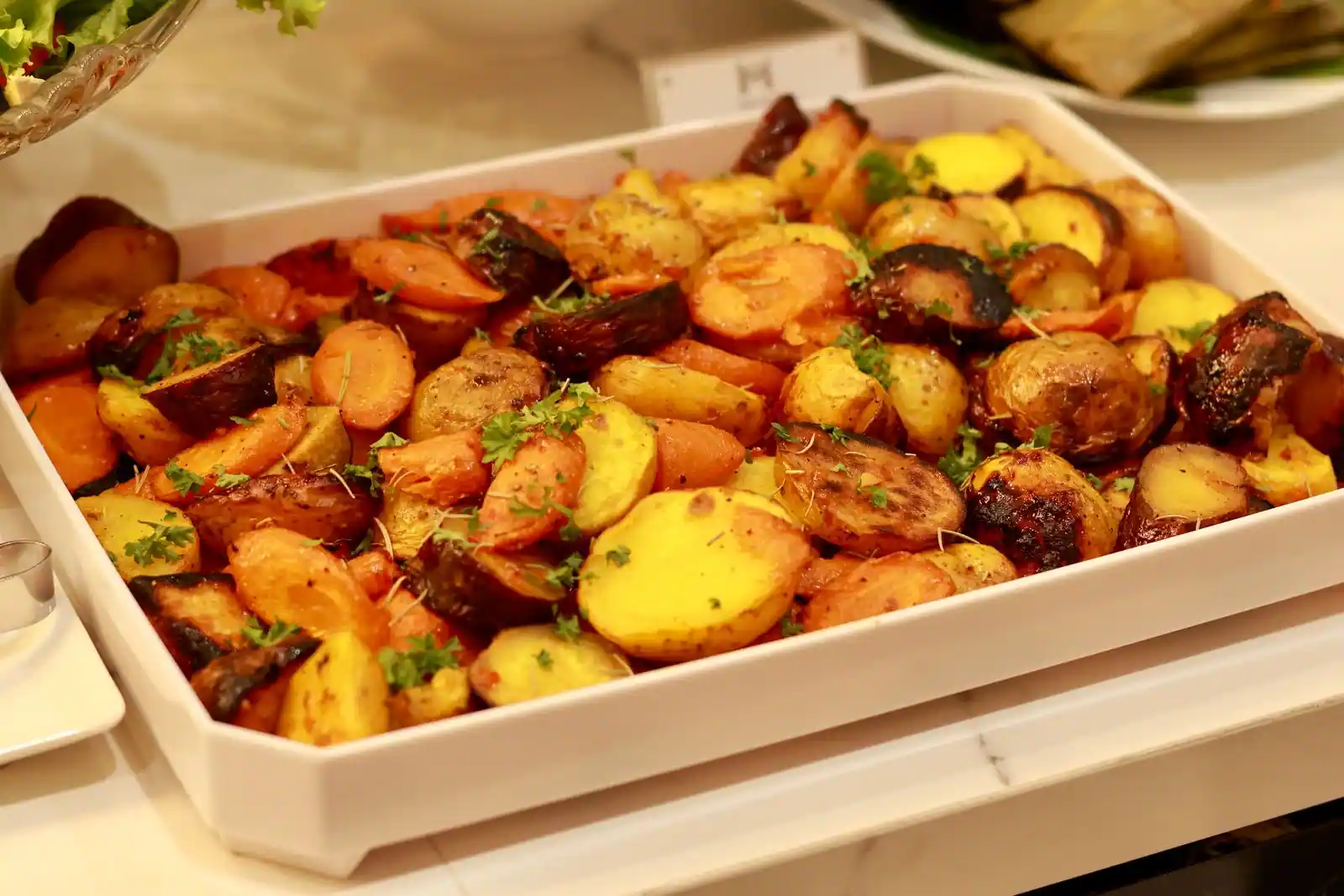 Pommes de terre, carottes et patates douces rôties au four, parsemées d'herbes, dans un plat de service.
