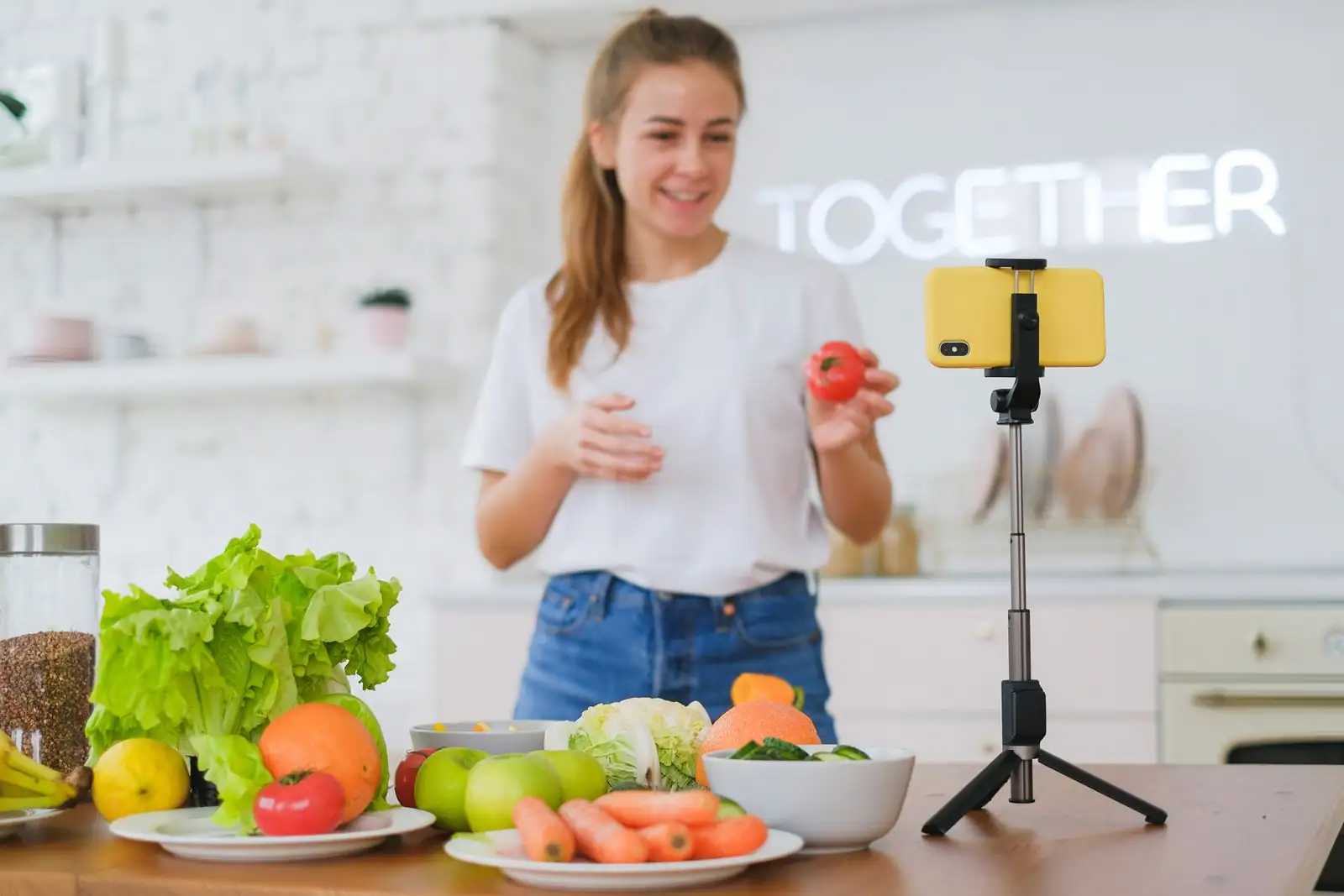 Une créatrice filme une séquence de cuisine au smartphone, devant des légumes et des fruits frais.