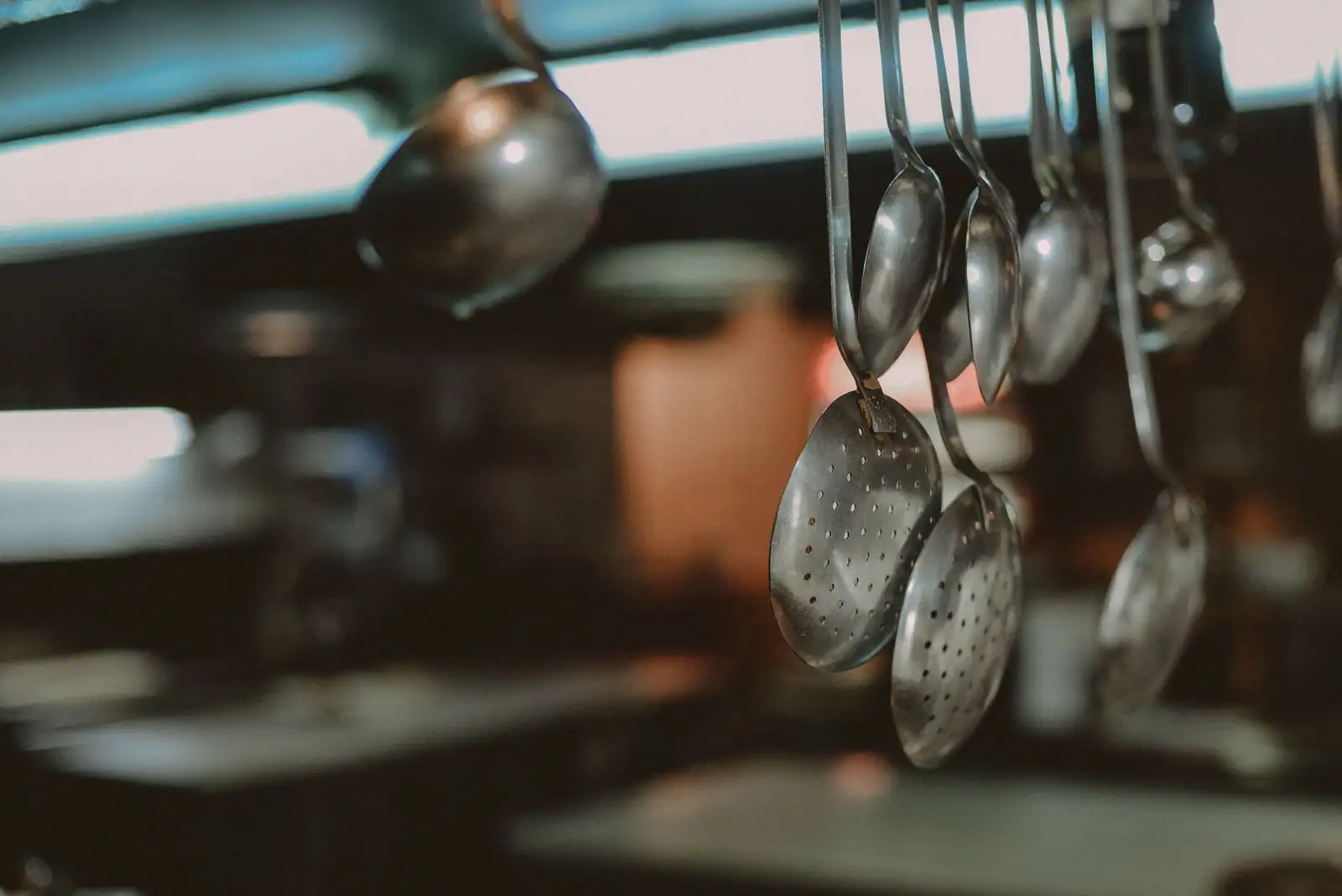 Louches et écumoires en métal suspendues à une barre, dans une cuisine de restaurant.