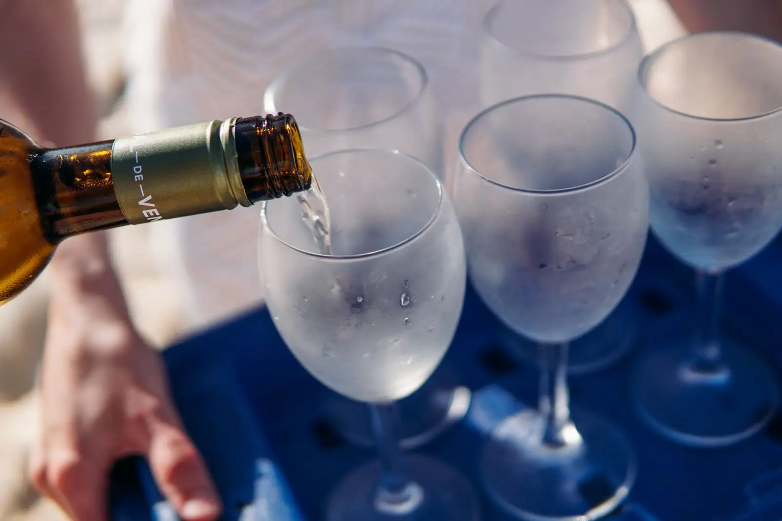 Une bouteille verse du vin blanc dans une série de verres à pied embués posés sur un plateau