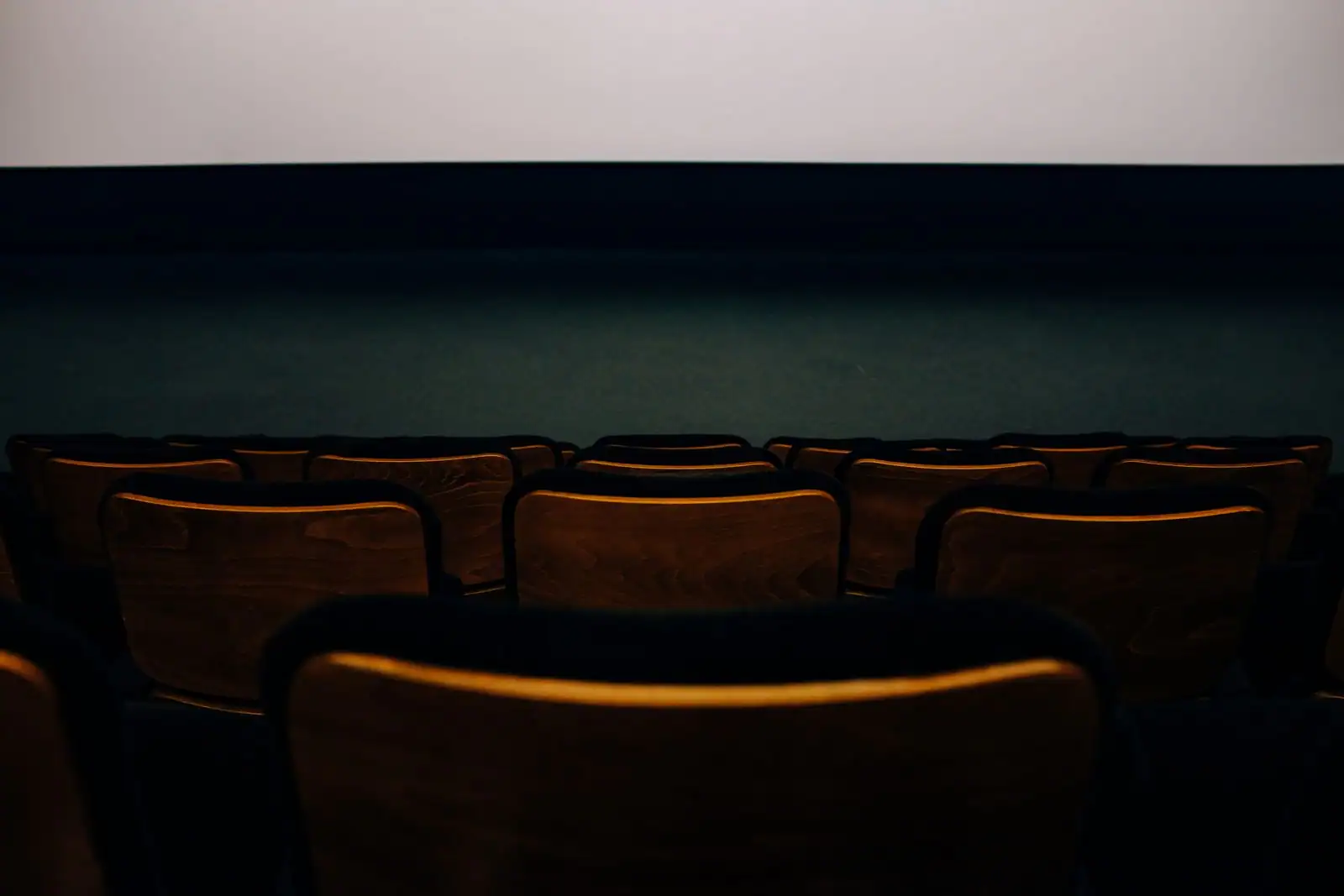 Salle de cinéma vide, rangées de fauteuils tournées vers l'écran éclairé dans la pénombre