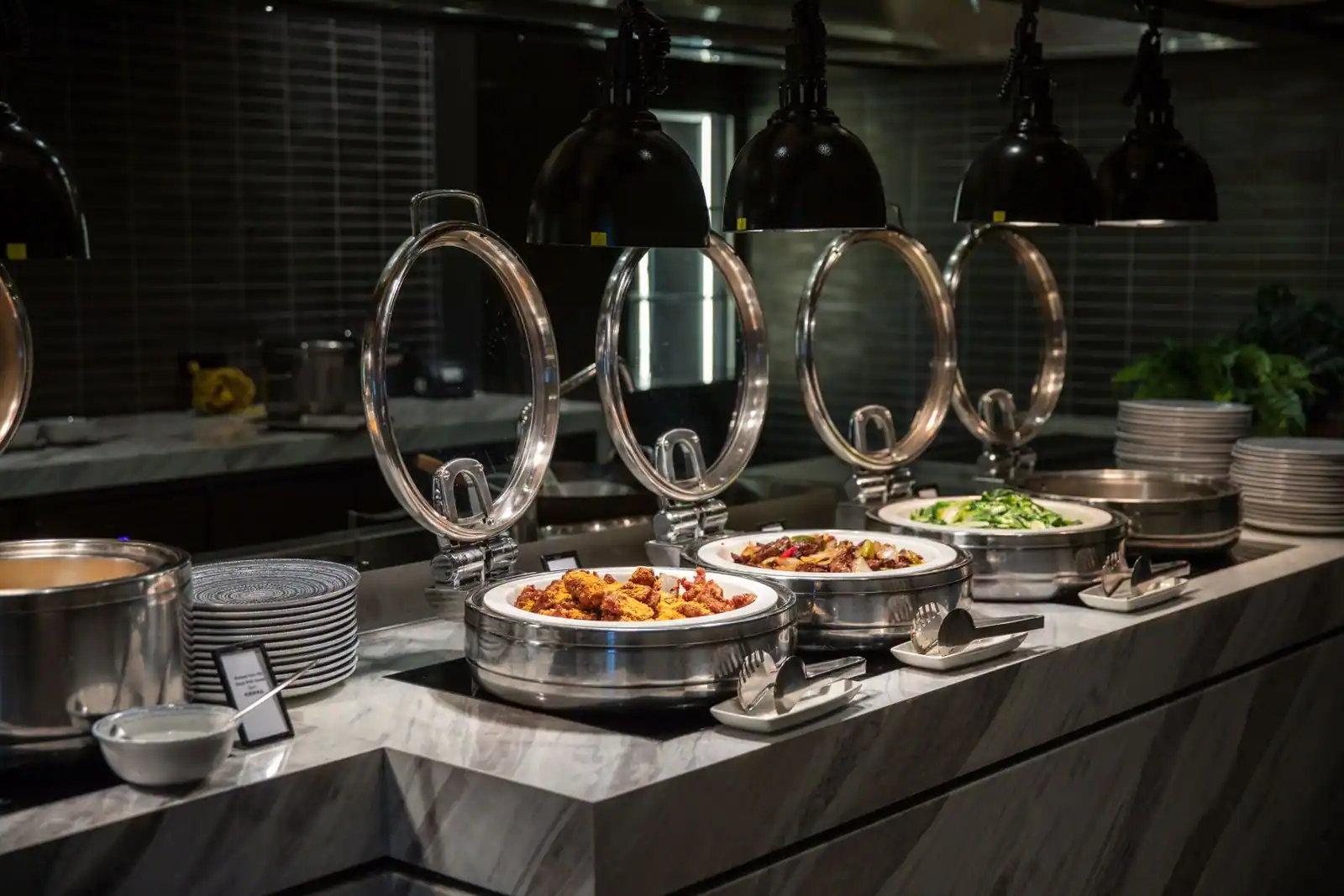 Comptoir de buffet en libre-service : bacs chauffants sous lampes, couverts de service et assiettes empilées