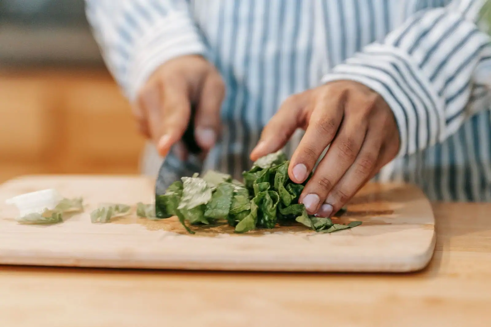 Couteau de cuisine utilisé pour couper des légumes verts sur une planche à découper en bois.