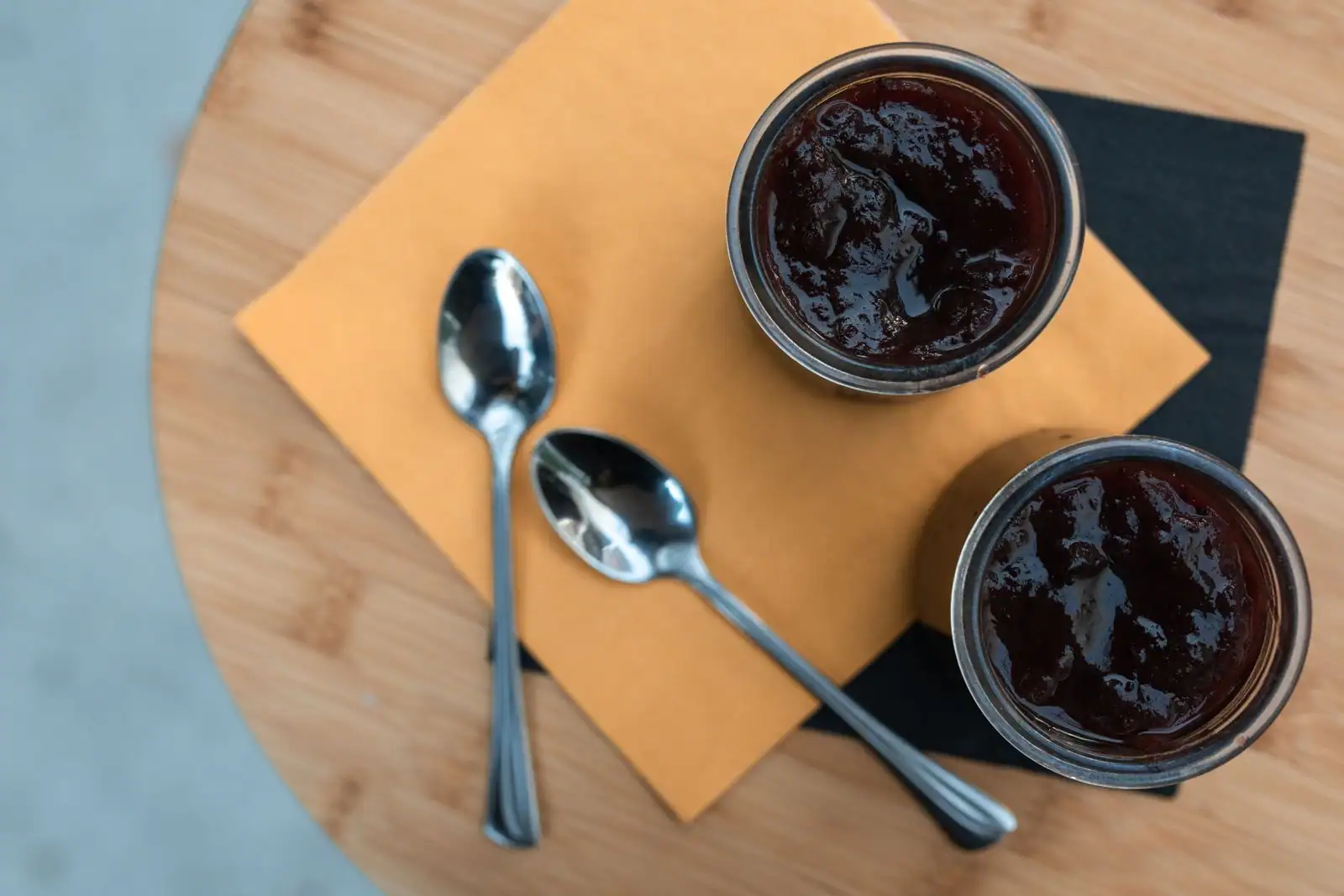 Deux petits pots individuels de dessert aux fruits rouges, avec des cuillères, posés sur une table en bois.
