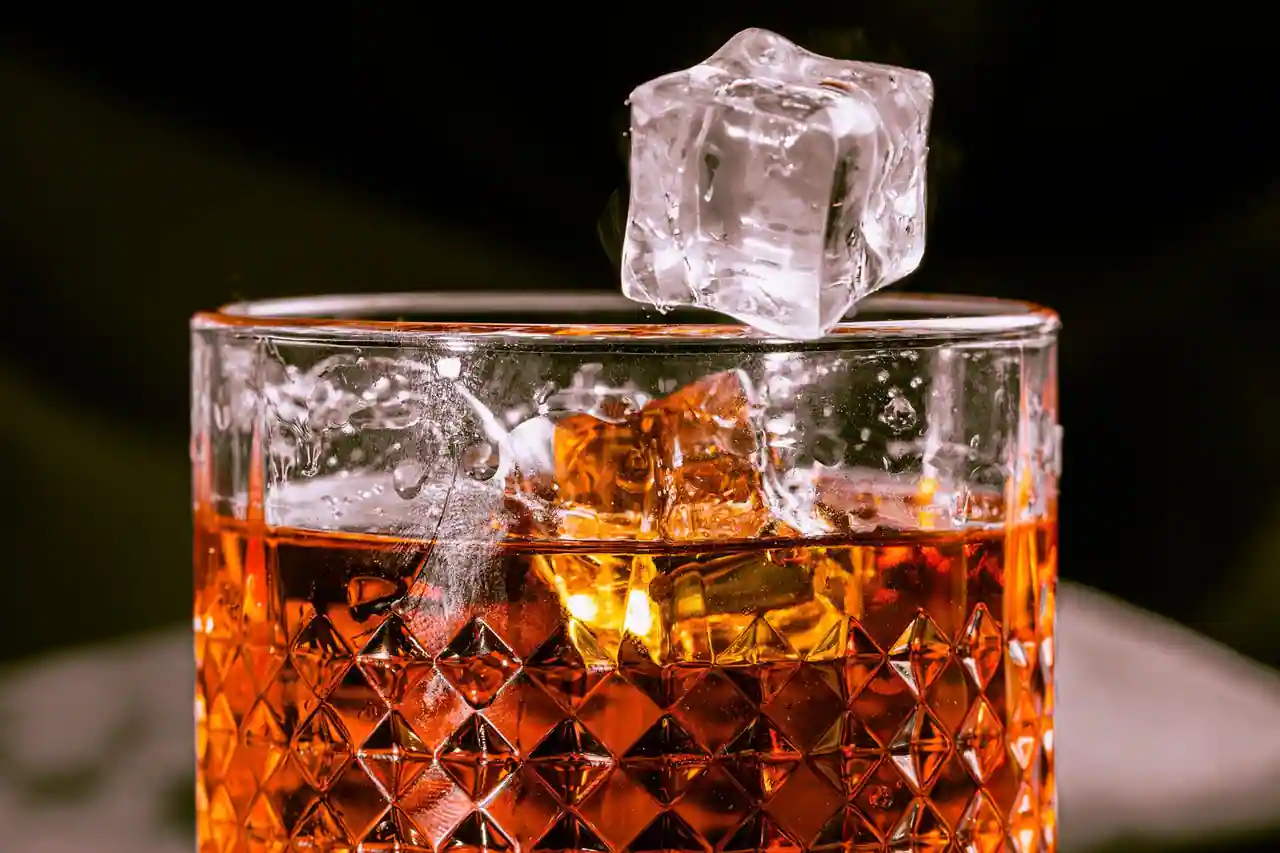 Verre de whisky ambré avec un glaçon, servi sur fond sombre, gros plan sur la dégustation.