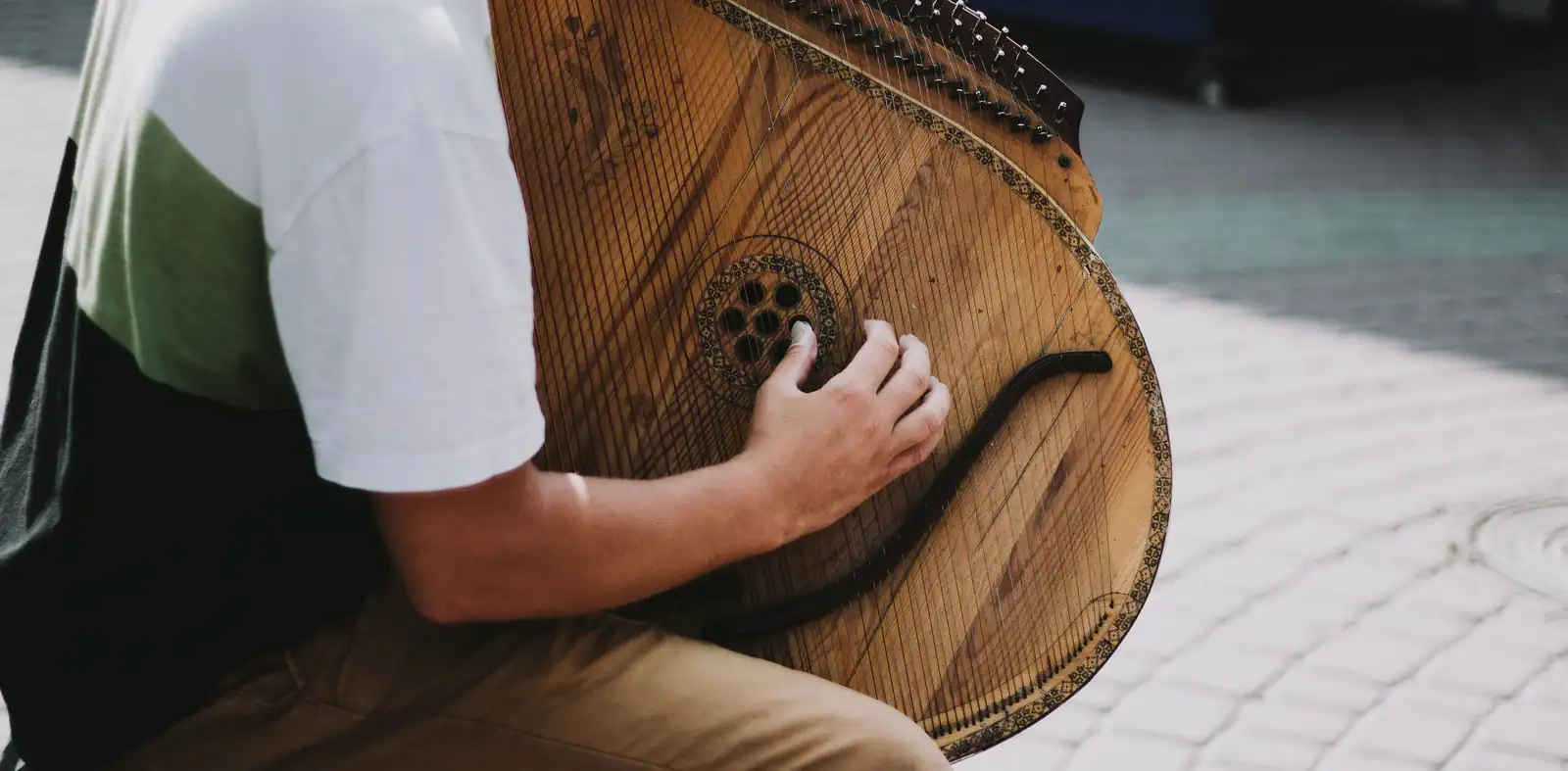 Musicien de rue jouant un instrument traditionnel à cordes en bois, image illustrative sans lien direct avec la vielle à roue