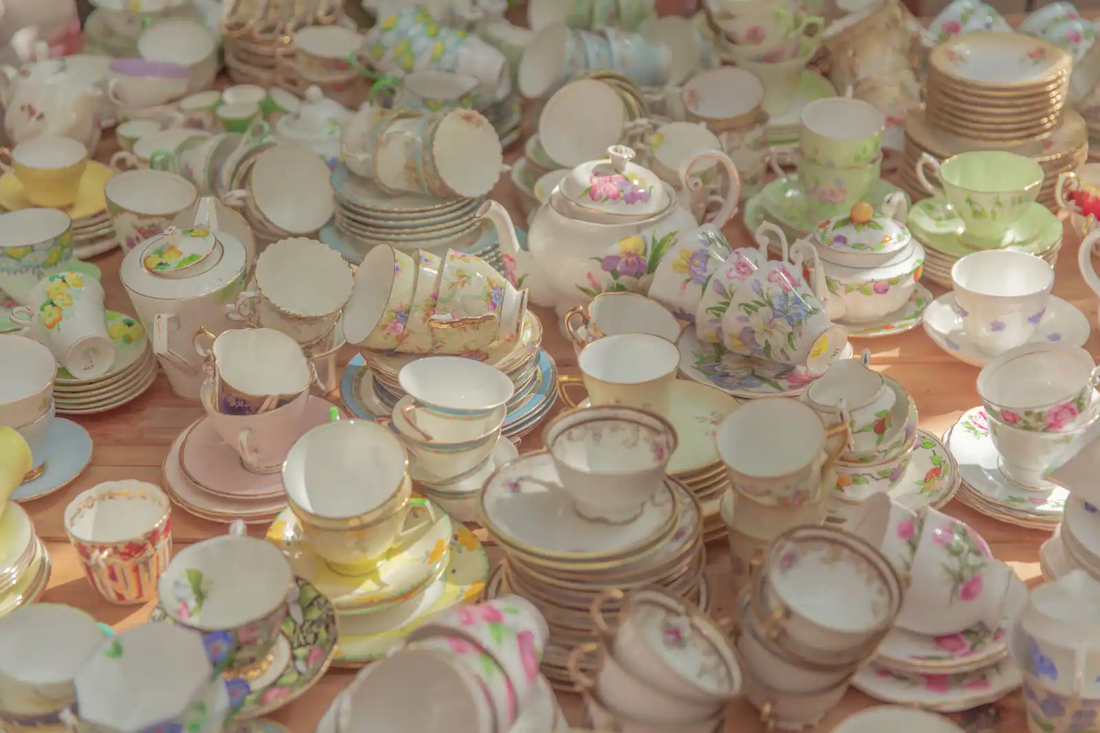 Collection de tasses, soucoupes et théières en porcelaine ancienne à motifs floraux et filets dorés, disposées sur une table en bois