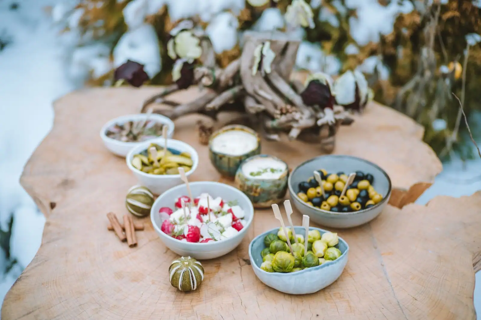 Assortiment de petites entrées froides, olives, pickles et feta, servies dans des bols sur une table en bois.