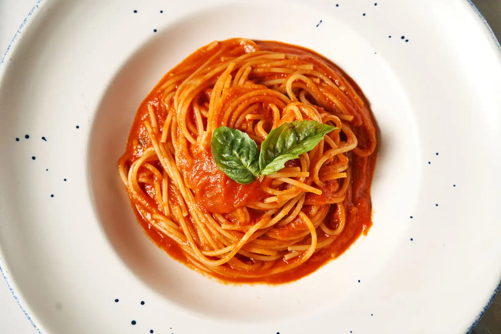 Spaghetti nappés d'une sauce tomate onctueuse et brillante, garnis de basilic frais, servis dans une assiette blanche