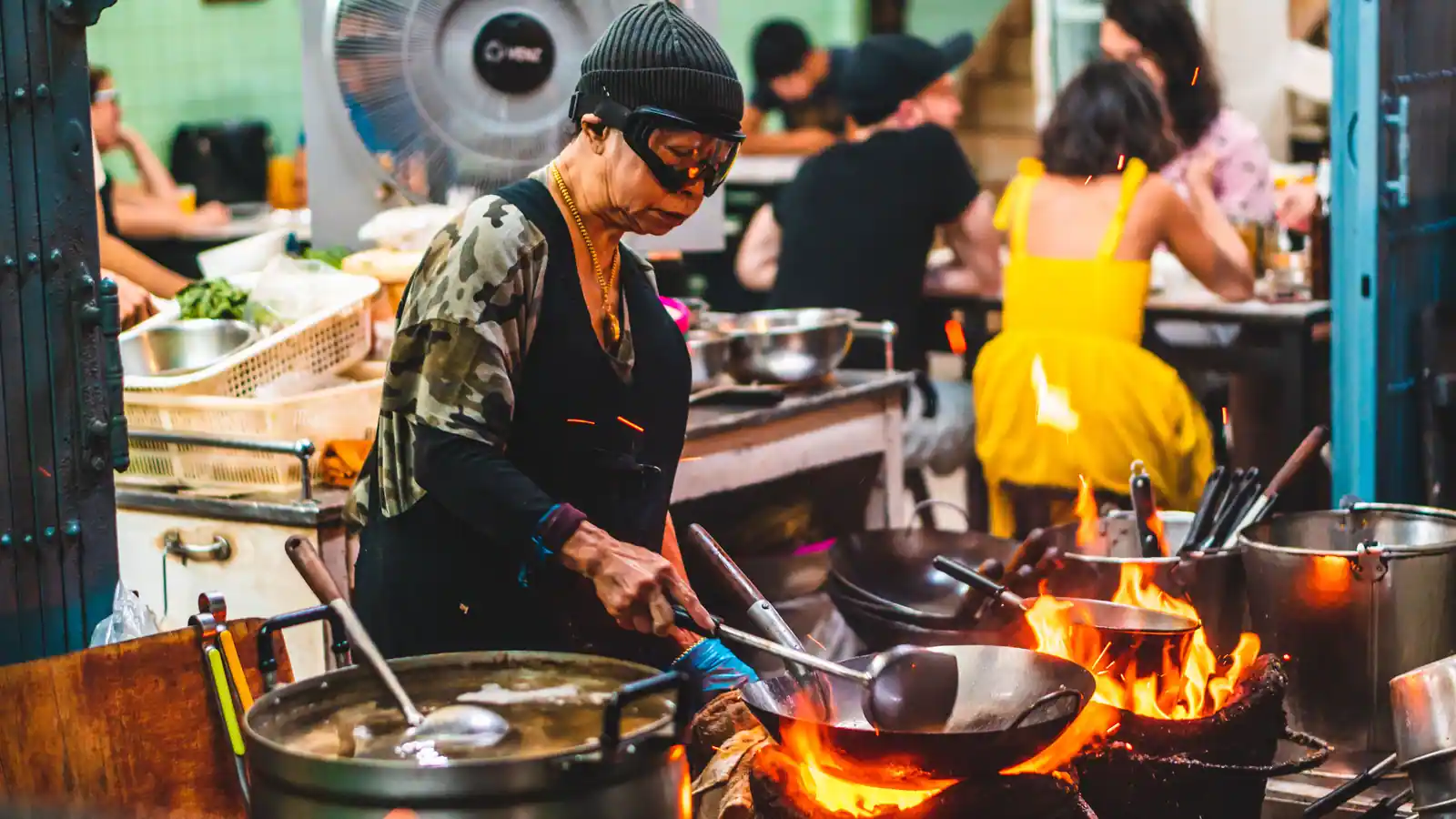 Une cuisinière fait sauter des ingrédients dans un wok au-dessus d'un feu vif, cuisine animée.